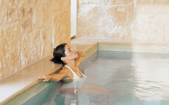 A woman sits in a pool with her arms outstretched. She looks relaxed as she leans her head back.